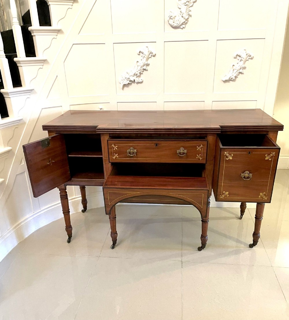 A Regency period mahogany breakfront sideboard featuring brass inlay motifs, a central drawer flanked by cupboards, turned legs, and brass castors. View XII