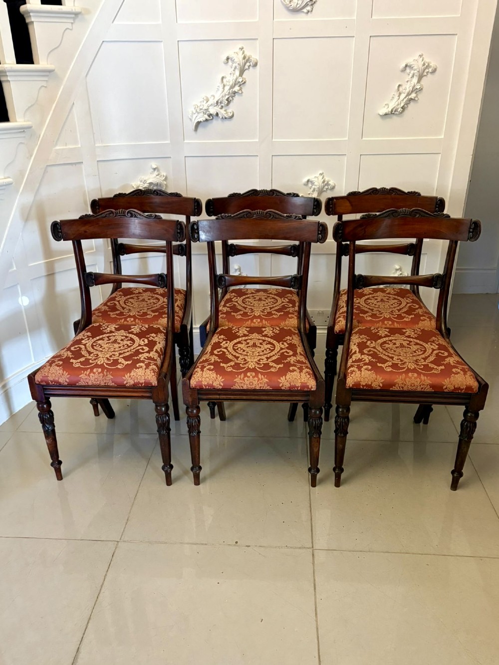 A set of six Regency carved rosewood dining chairs featuring curved backrests with scroll details, turned front legs, and pattern-upholstered seats.