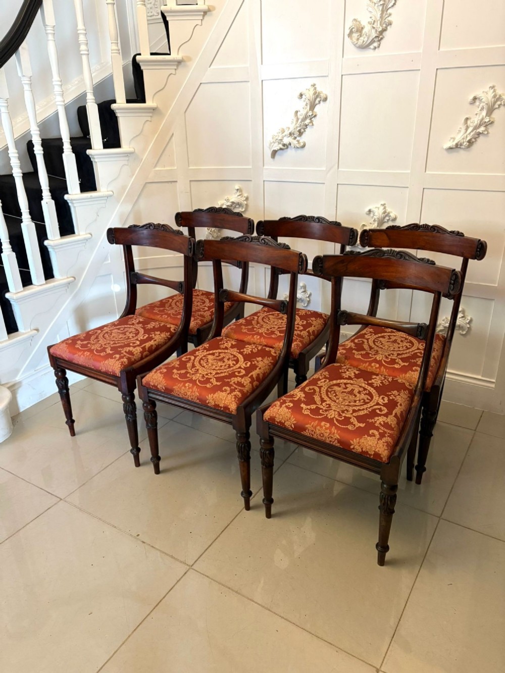 A set of six Regency carved rosewood dining chairs featuring curved backrests with scroll details, turned front legs, and pattern-upholstered seats. View X