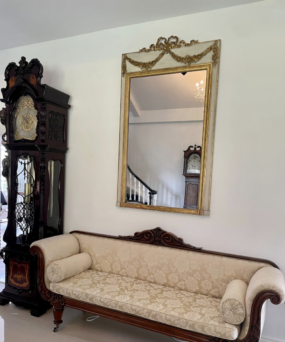A tall rectangular Victorian mirror featuring a white painted outer frame, gilded beaded inner border, and a gilded ribbon crest with floral swags. View IV