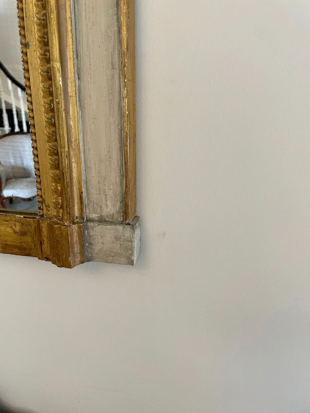 A tall rectangular Victorian mirror featuring a white painted outer frame, gilded beaded inner border, and a gilded ribbon crest with floral swags. View VIII