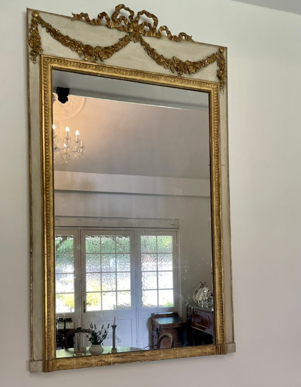 A tall rectangular Victorian mirror featuring a white painted outer frame, gilded beaded inner border, and a gilded ribbon crest with floral swags. View XI