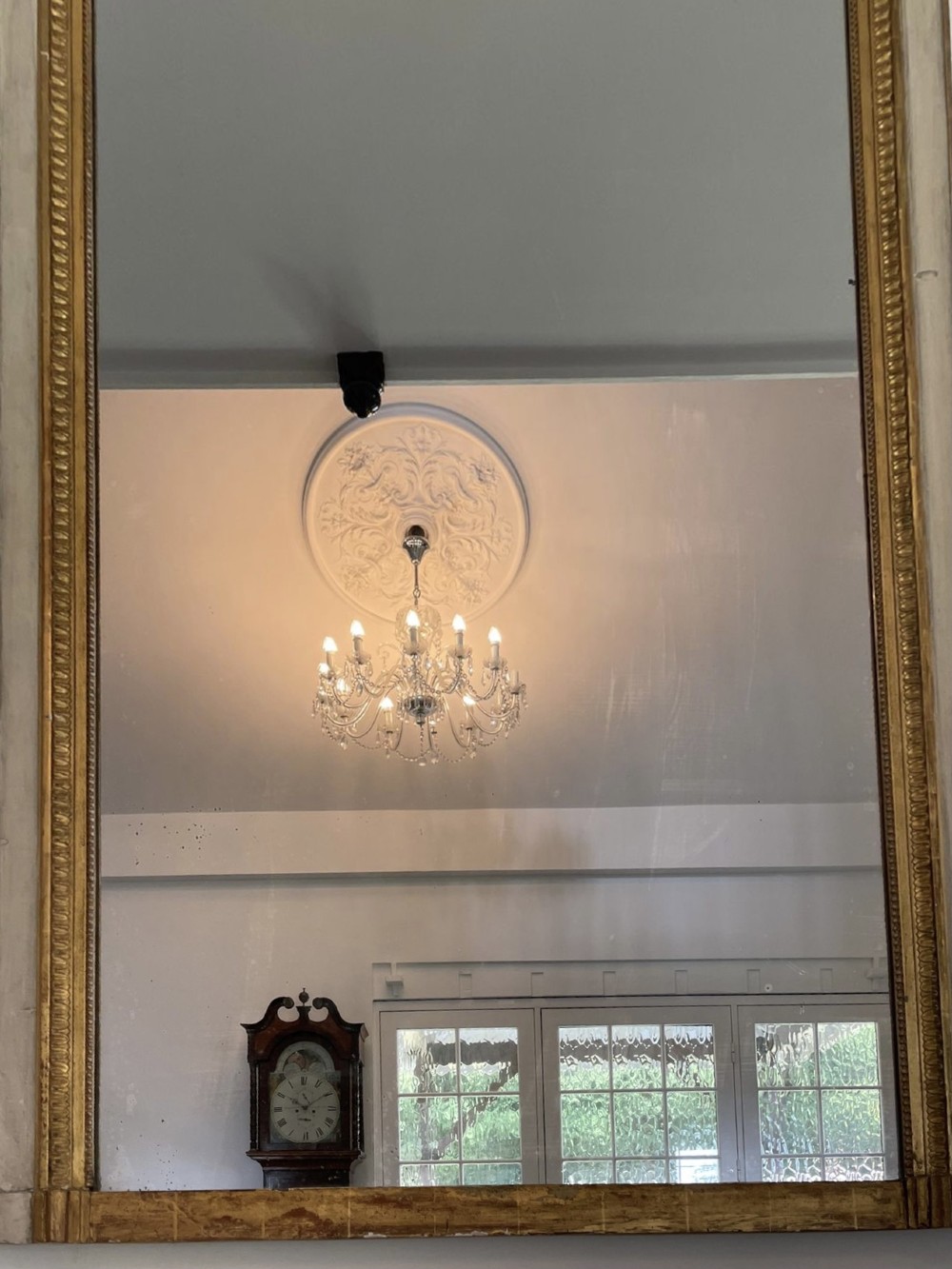 A tall rectangular Victorian mirror featuring a white painted outer frame, gilded beaded inner border, and a gilded ribbon crest with floral swags. View XII