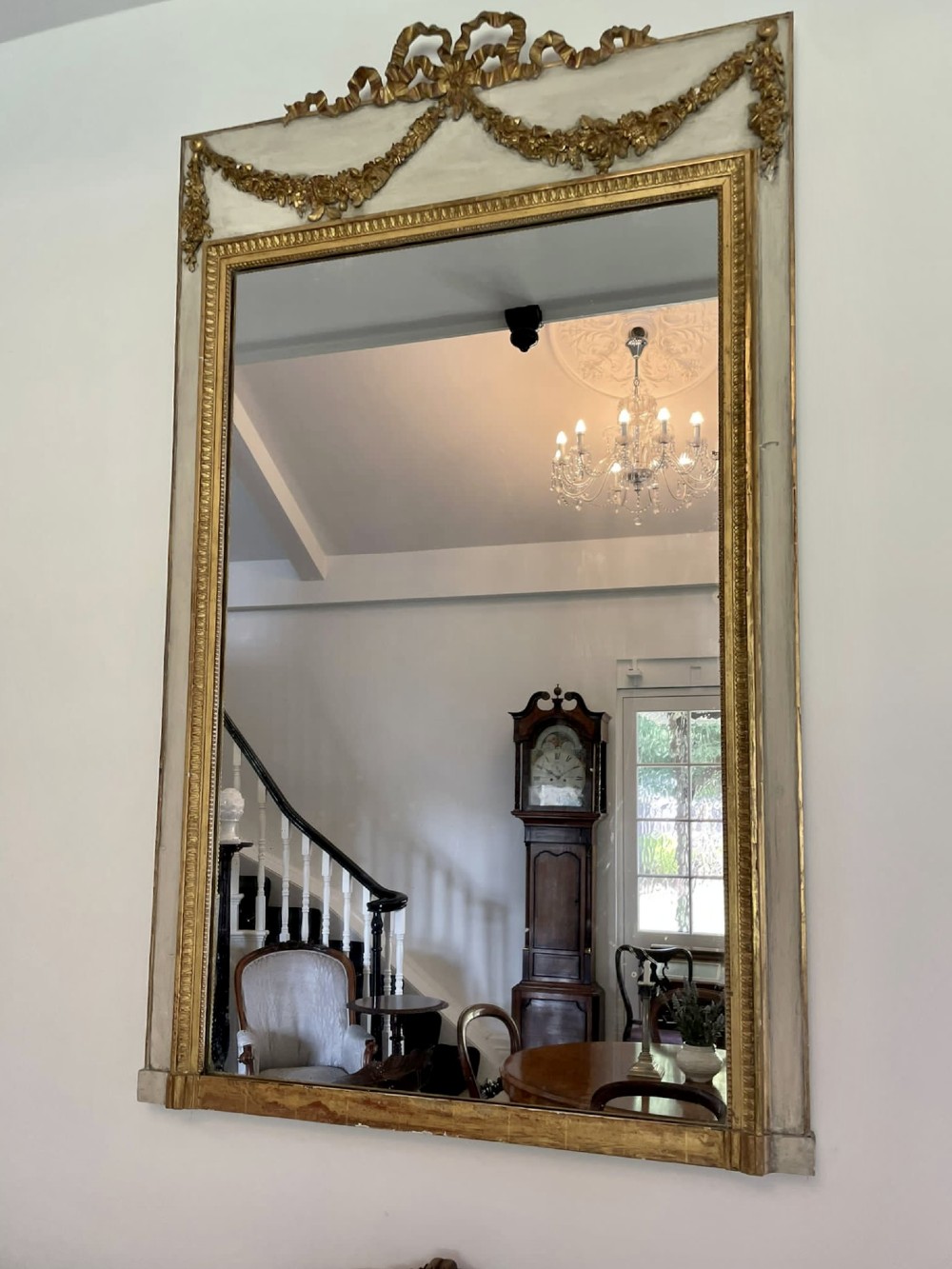 A tall rectangular Victorian mirror featuring a white painted outer frame, gilded beaded inner border, and a gilded ribbon crest with floral swags. View XIII