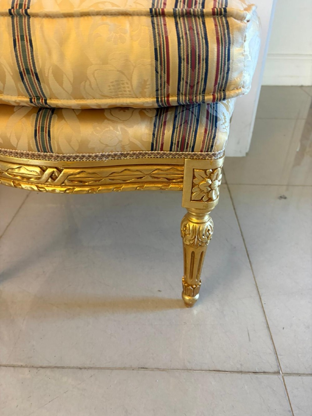 A pair of square French style footstools featuring carved gold giltwood frames, fluted legs, and yellow patterned upholstery. View V