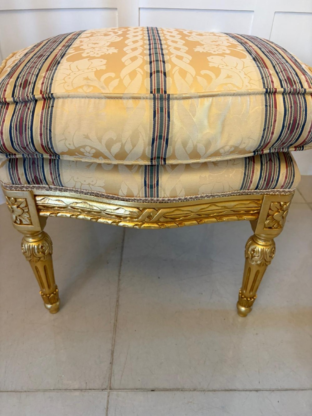 A pair of square French style footstools featuring carved gold giltwood frames, fluted legs, and yellow patterned upholstery. View X