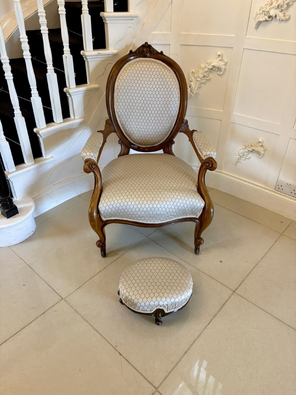 An eleven-piece antique Victorian carved walnut salon suite featuring a central sofa, pair of armchairs, six side chairs, and two footstools, all upholstered in a patterned cream fabric. View IV