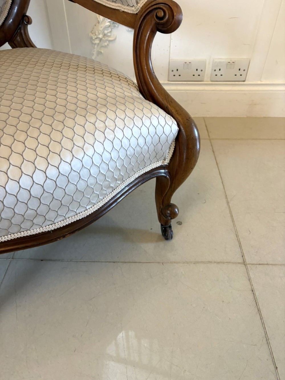 An eleven-piece antique Victorian carved walnut salon suite featuring a central sofa, pair of armchairs, six side chairs, and two footstools, all upholstered in a patterned cream fabric. View V