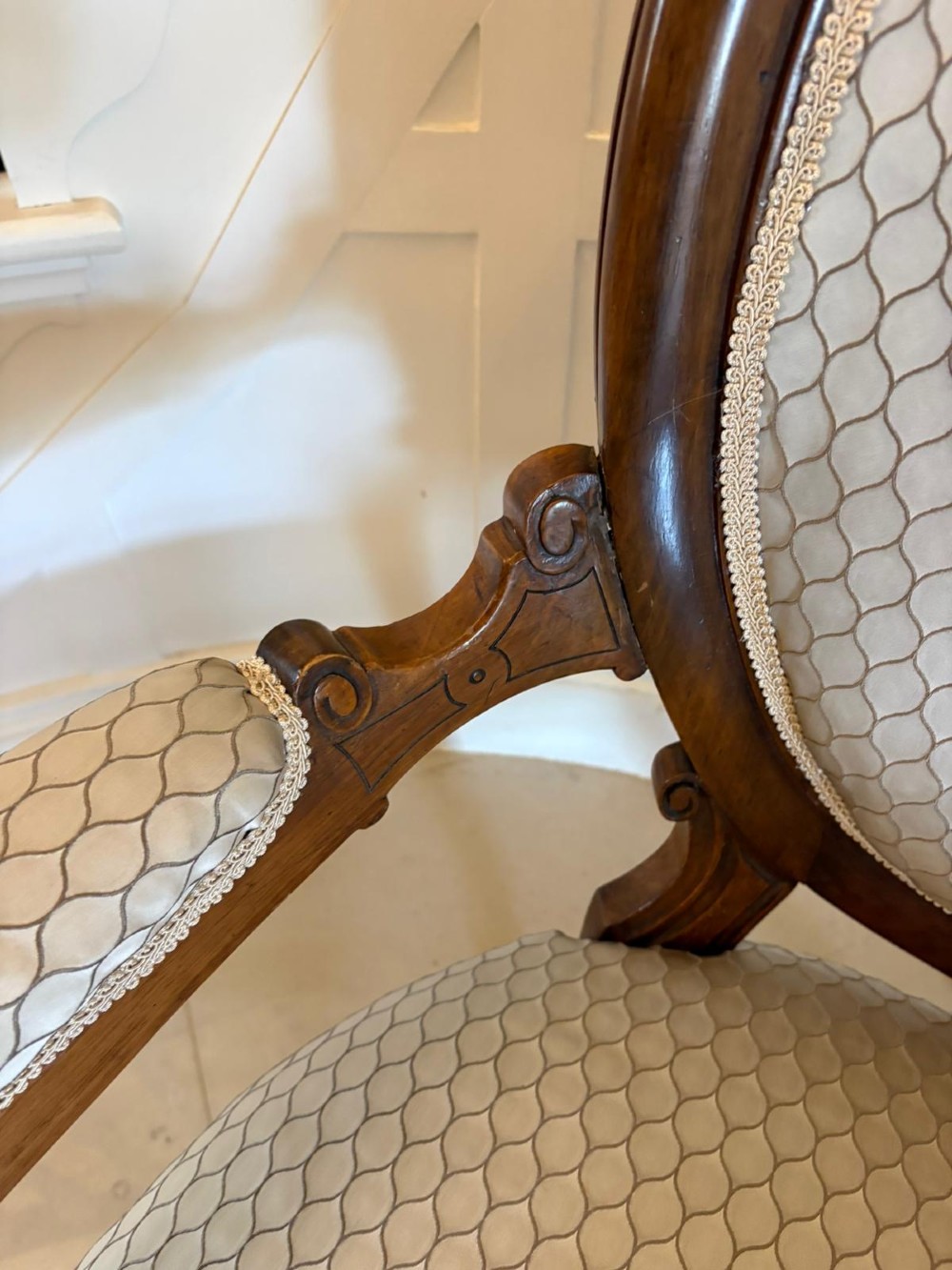An eleven-piece antique Victorian carved walnut salon suite featuring a central sofa, pair of armchairs, six side chairs, and two footstools, all upholstered in a patterned cream fabric. View VI