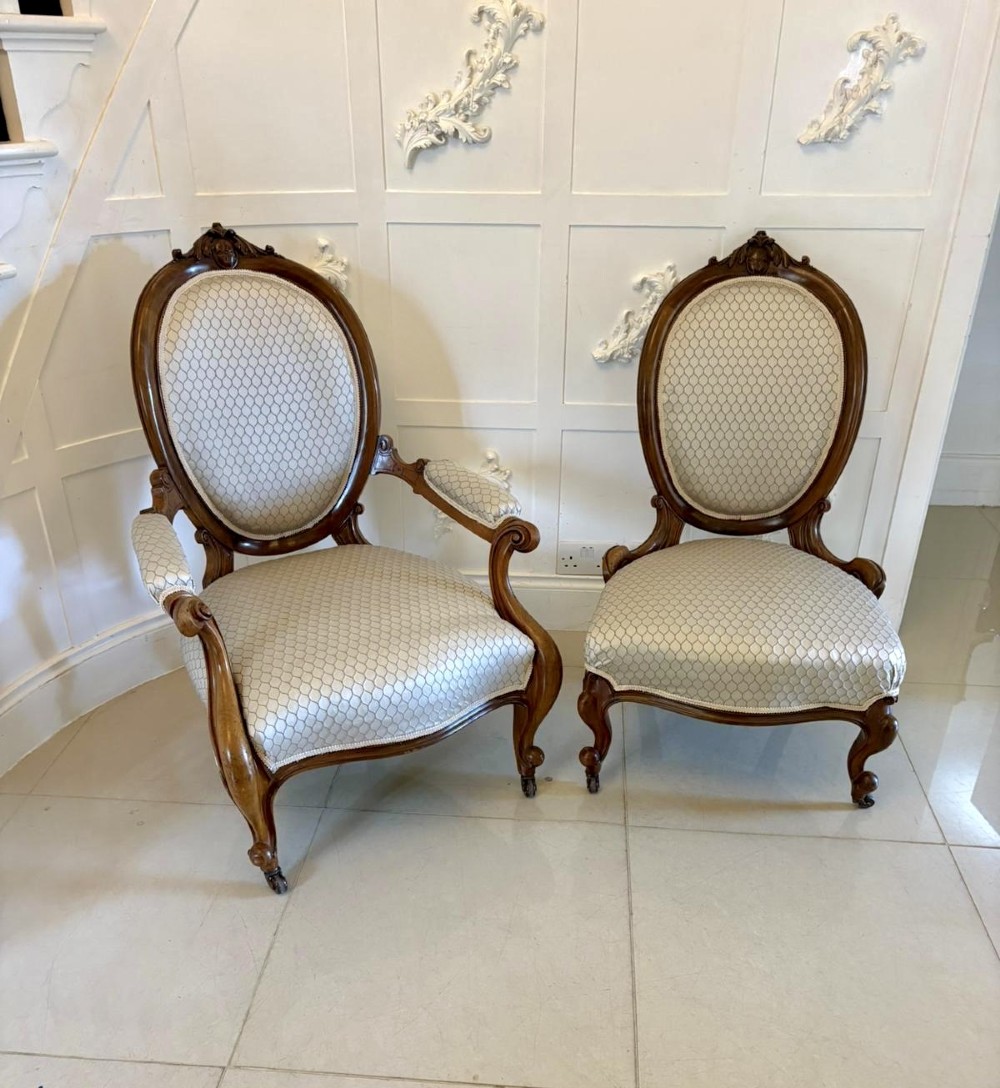 An eleven-piece antique Victorian carved walnut salon suite featuring a central sofa, pair of armchairs, six side chairs, and two footstools, all upholstered in a patterned cream fabric. View VII