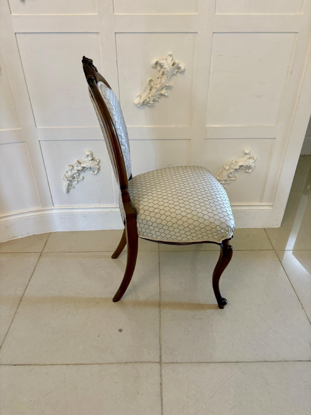 An eleven-piece antique Victorian carved walnut salon suite featuring a central sofa, pair of armchairs, six side chairs, and two footstools, all upholstered in a patterned cream fabric. View IX