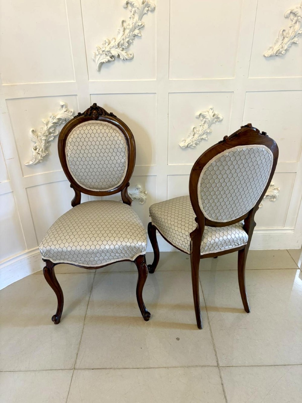 An eleven-piece antique Victorian carved walnut salon suite featuring a central sofa, pair of armchairs, six side chairs, and two footstools, all upholstered in a patterned cream fabric. View X