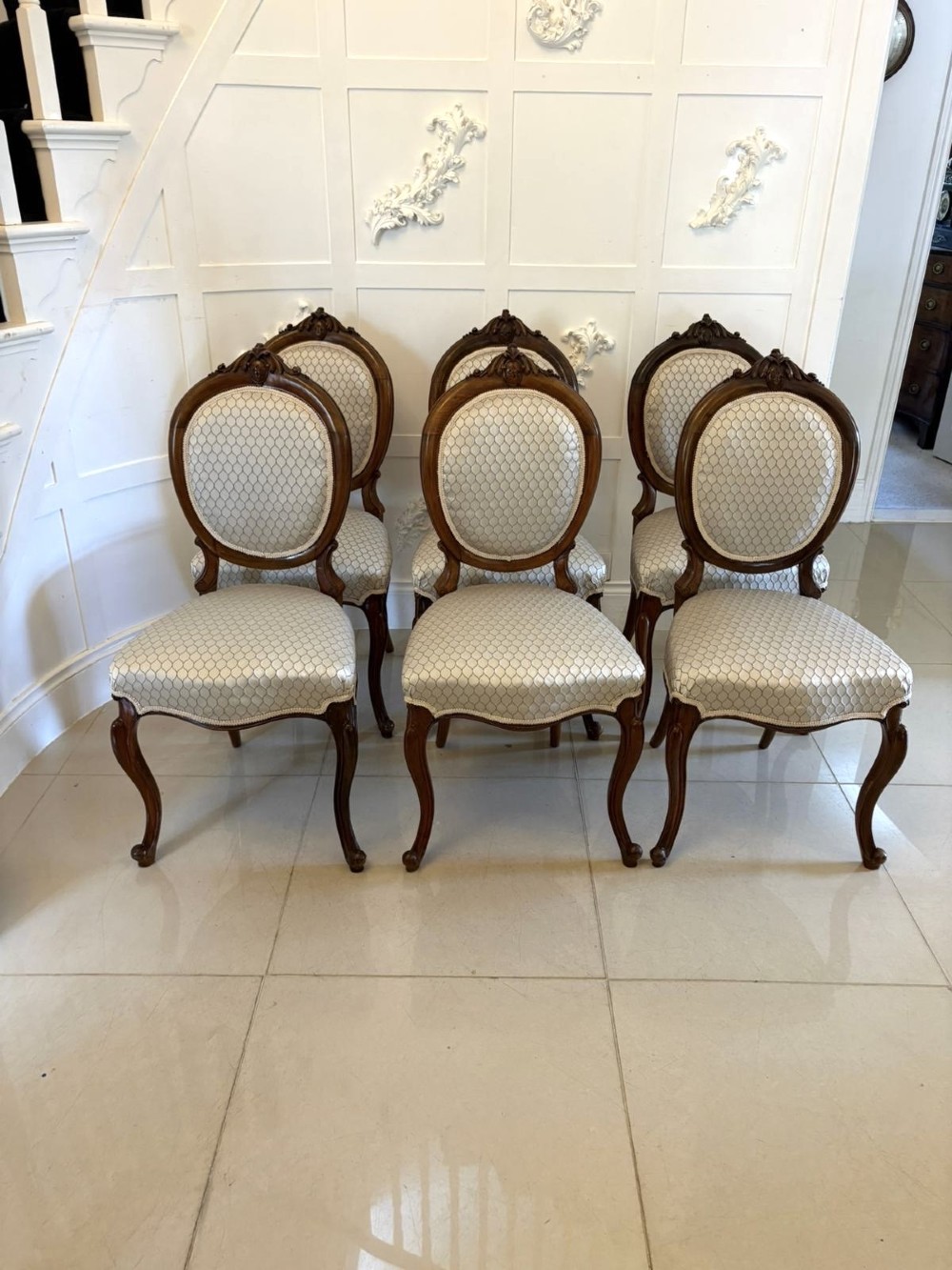 An eleven-piece antique Victorian carved walnut salon suite featuring a central sofa, pair of armchairs, six side chairs, and two footstools, all upholstered in a patterned cream fabric. View XI