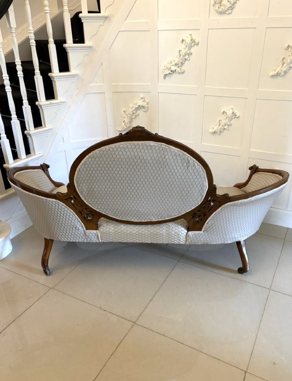 An eleven-piece antique Victorian carved walnut salon suite featuring a central sofa, pair of armchairs, six side chairs, and two footstools, all upholstered in a patterned cream fabric. View XII