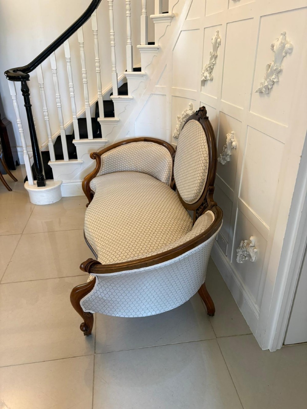 An eleven-piece antique Victorian carved walnut salon suite featuring a central sofa, pair of armchairs, six side chairs, and two footstools, all upholstered in a patterned cream fabric. View XIII