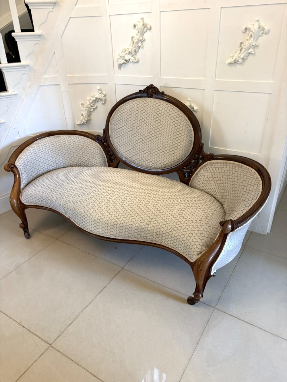 An eleven-piece antique Victorian carved walnut salon suite featuring a central sofa, pair of armchairs, six side chairs, and two footstools, all upholstered in a patterned cream fabric. View XIV