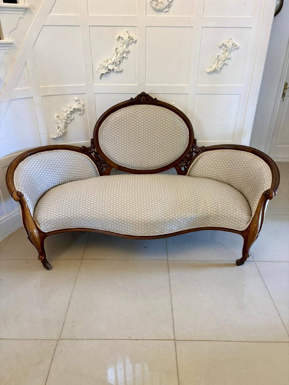 An eleven-piece antique Victorian carved walnut salon suite featuring a central sofa, pair of armchairs, six side chairs, and two footstools, all upholstered in a patterned cream fabric. View XV
