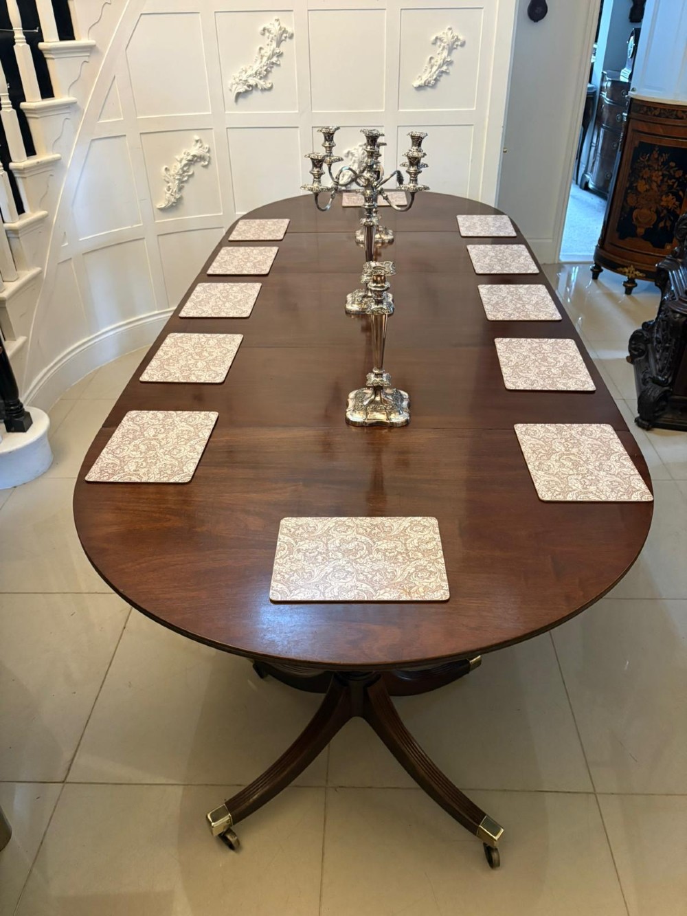 A large mahogany extending dining table featuring an oval surface with two additional leaves, supported by splayed pedestal legs with brass castors. View III