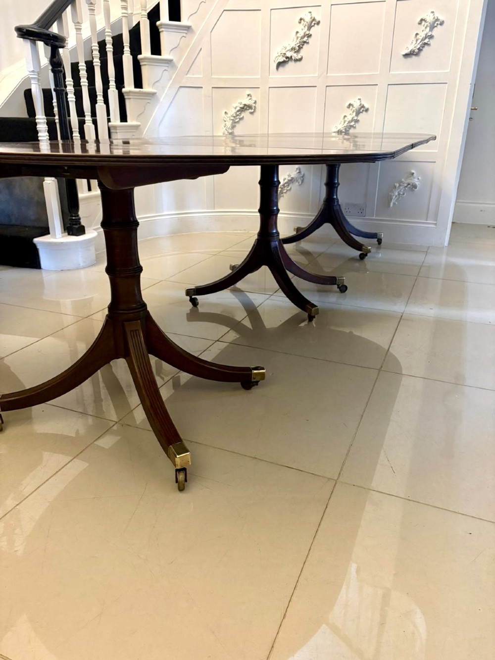 A large mahogany extending dining table featuring an oval surface with two additional leaves, supported by splayed pedestal legs with brass castors. View V