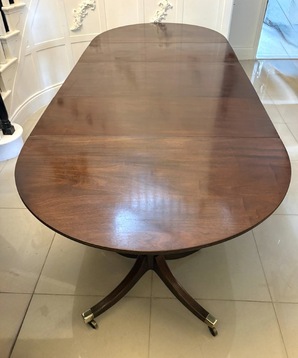 A large mahogany extending dining table featuring an oval surface with two additional leaves, supported by splayed pedestal legs with brass castors.