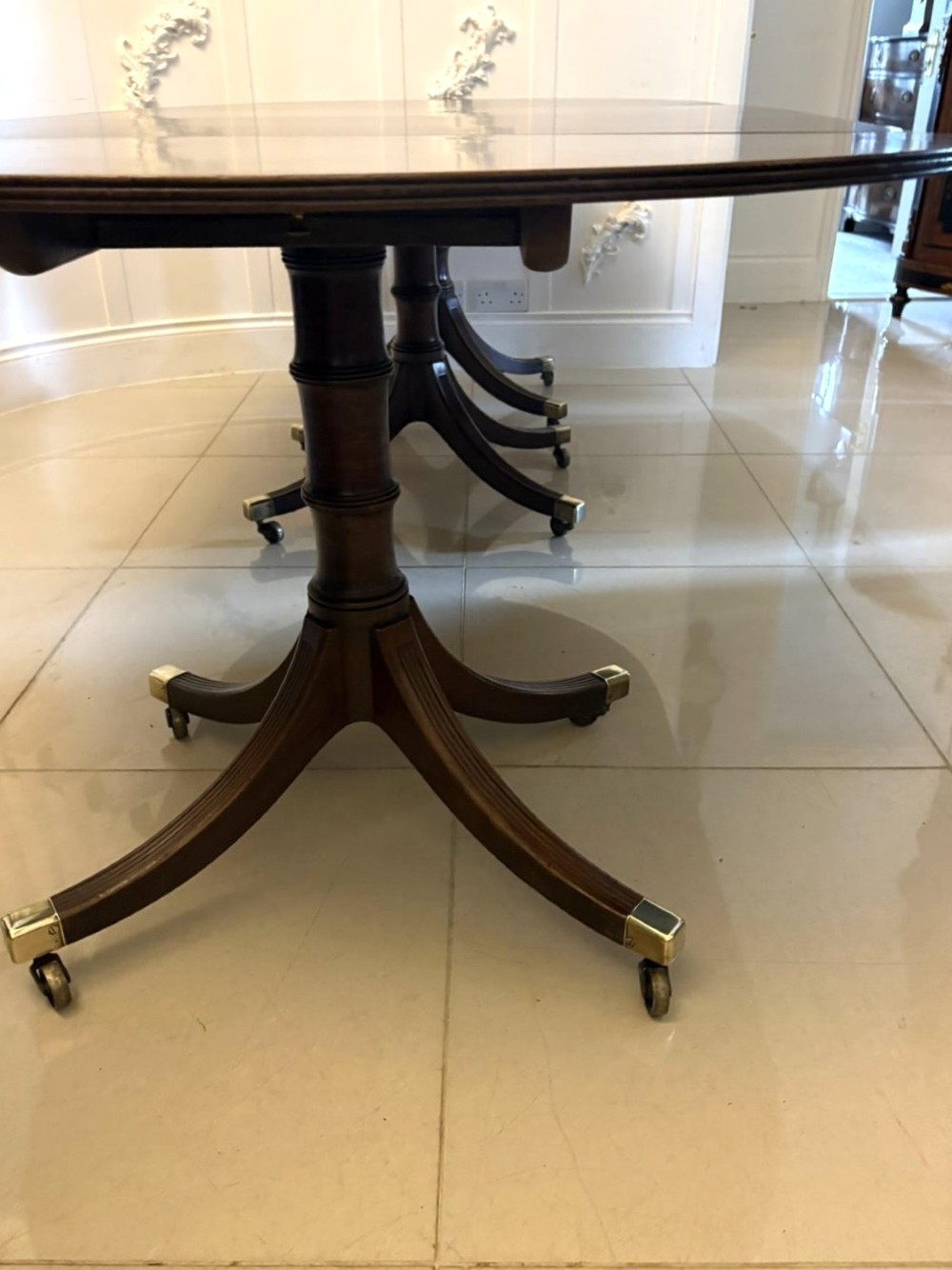 A large mahogany extending dining table featuring an oval surface with two additional leaves, supported by splayed pedestal legs with brass castors. View VIII
