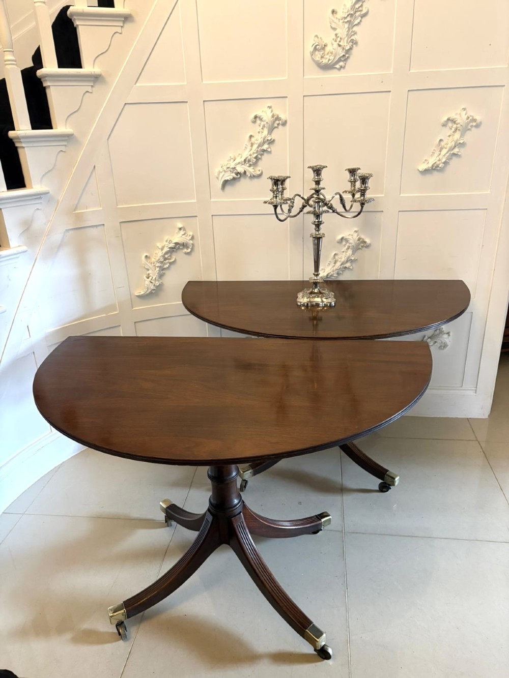 A large mahogany extending dining table featuring an oval surface with two additional leaves, supported by splayed pedestal legs with brass castors. View X