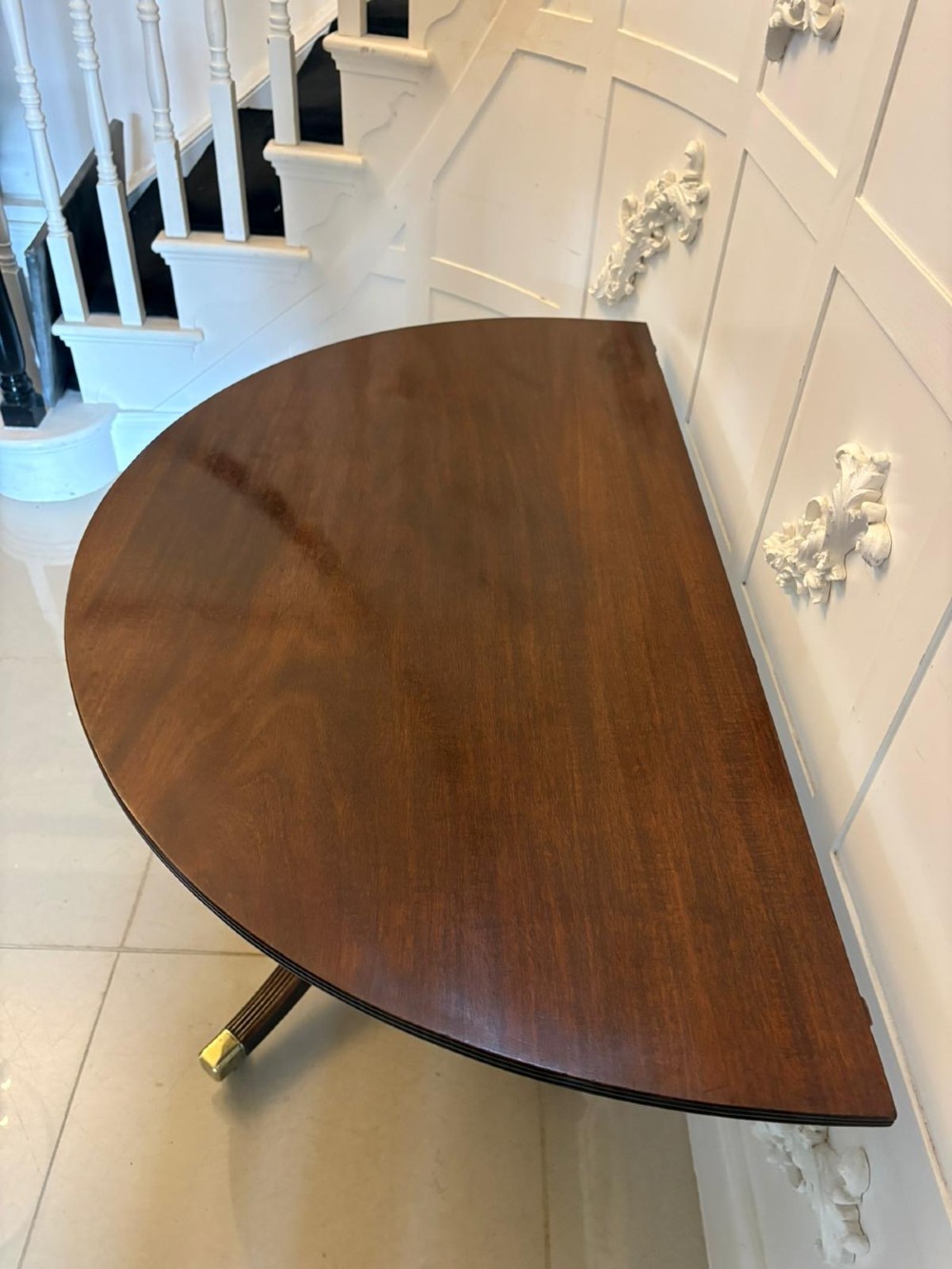 A large mahogany extending dining table featuring an oval surface with two additional leaves, supported by splayed pedestal legs with brass castors. View XI
