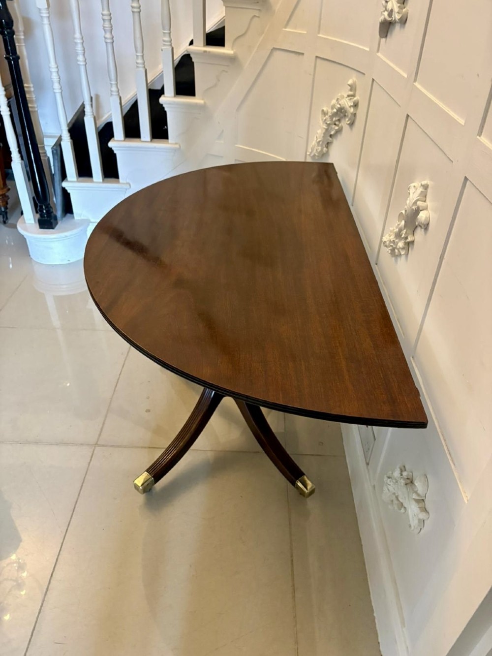 A large mahogany extending dining table featuring an oval surface with two additional leaves, supported by splayed pedestal legs with brass castors. View XII