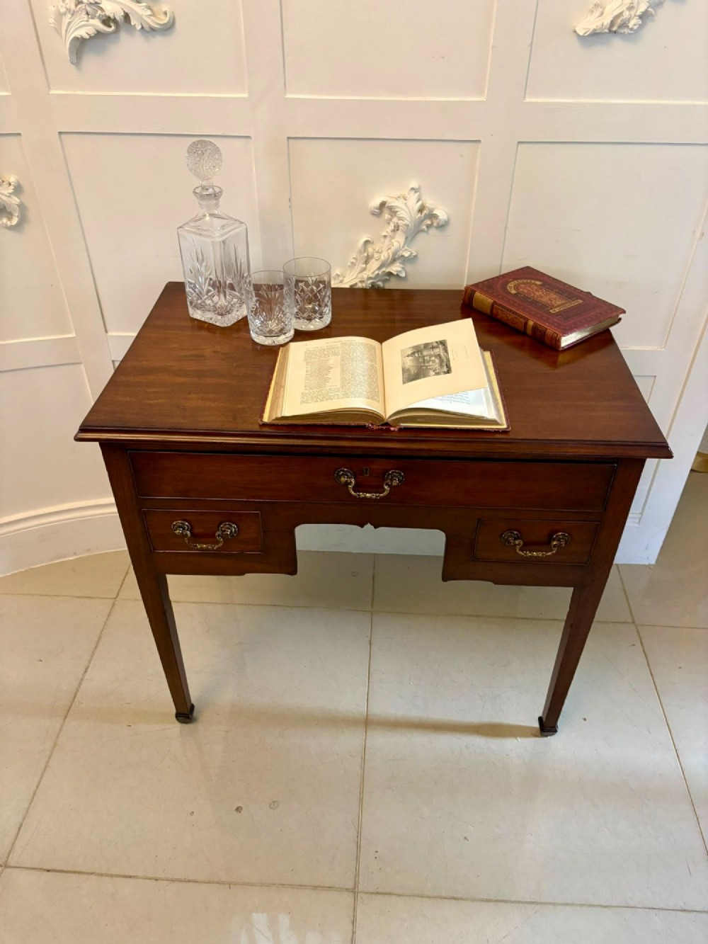 An antique Georgian mahogany lowboy hall table featuring three drawers with brass swan-neck handles and straight square legs. View V