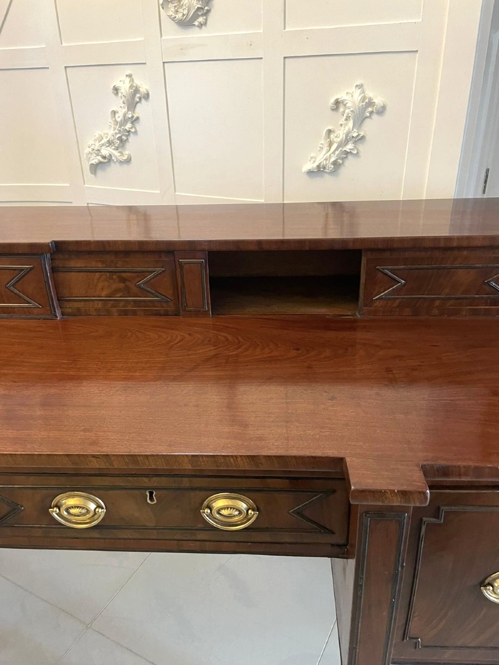 A large George III figured mahogany sideboard featuring a raised stage back, multiple drawers, side cupboards, brass ring handles, and turned reeded legs. View VIII
