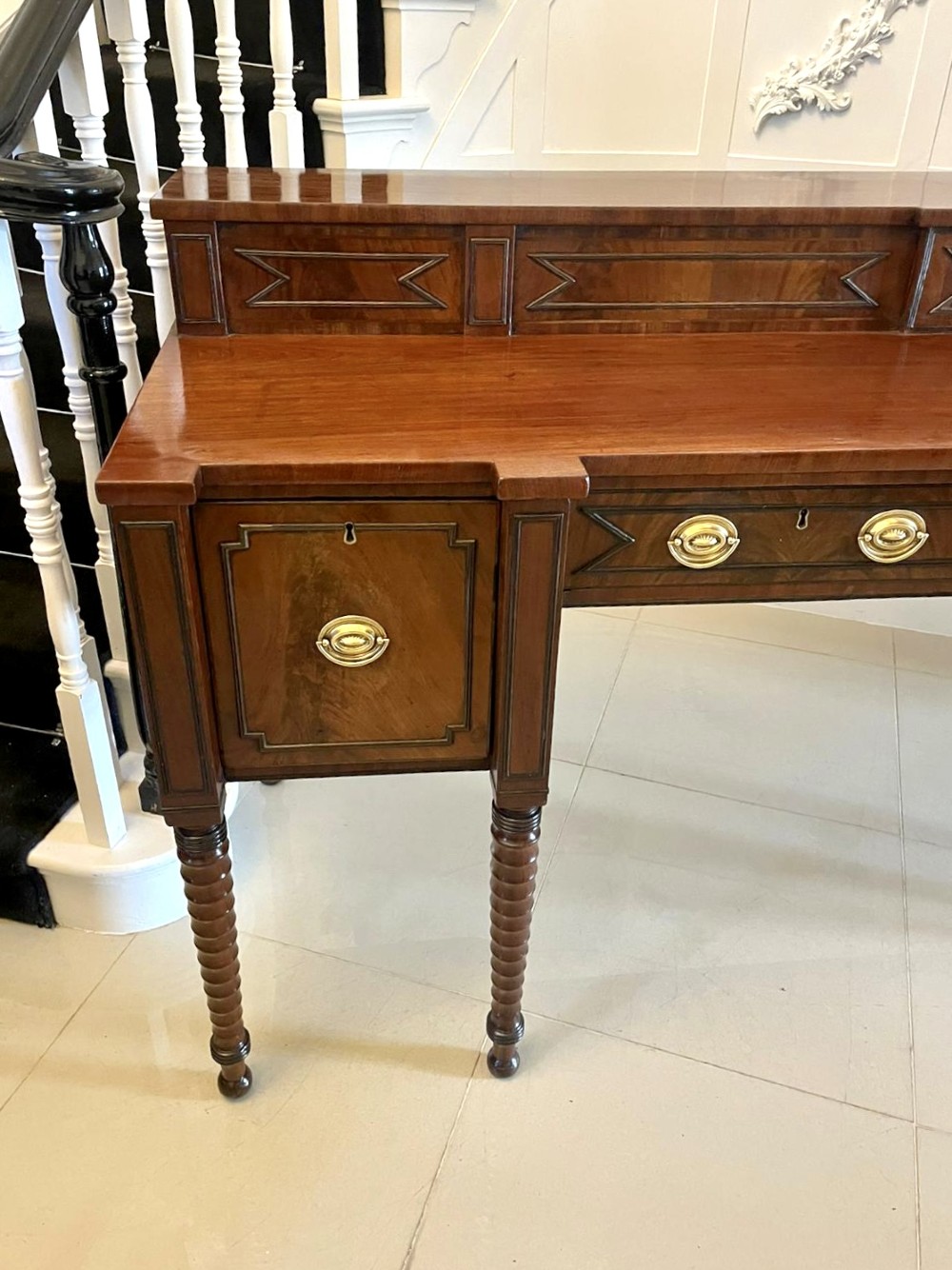 A large George III figured mahogany sideboard featuring a raised stage back, multiple drawers, side cupboards, brass ring handles, and turned reeded legs. View XII