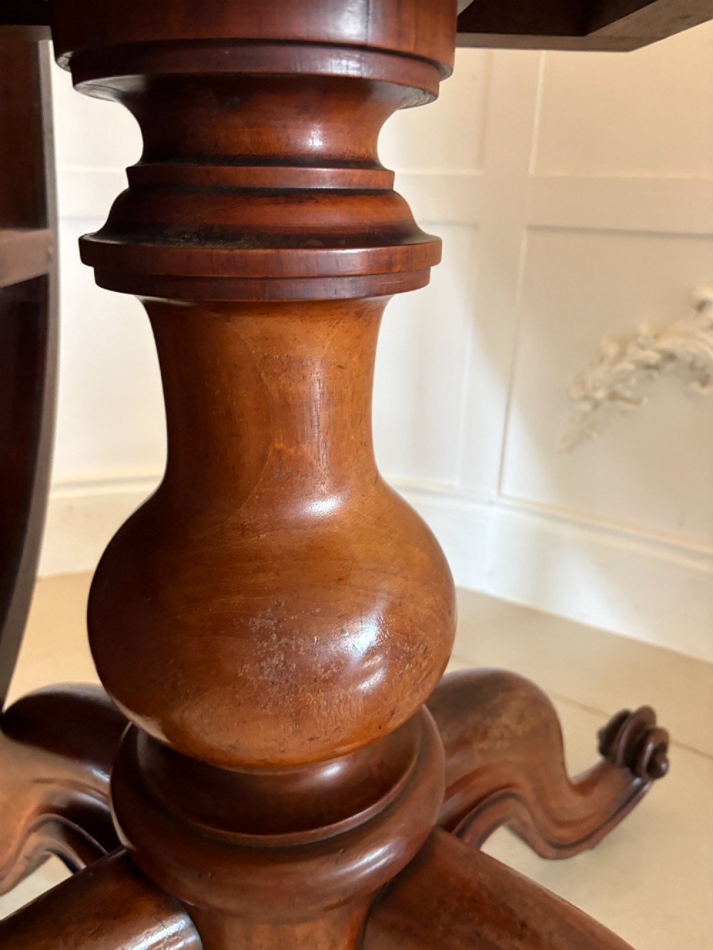 An oval Victorian tilt-top dining table in figured mahogany with satinwood crossbanding, set on a quadruped pedestal base with brass castors. View VI
