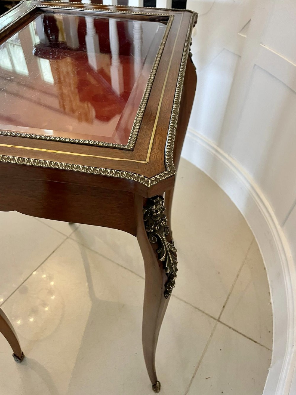 A 19th-century French mahogany bijouterie display table featuring a glazed top with brass inlay, a single front drawer, and slender cabriole legs with brass mounts. View V