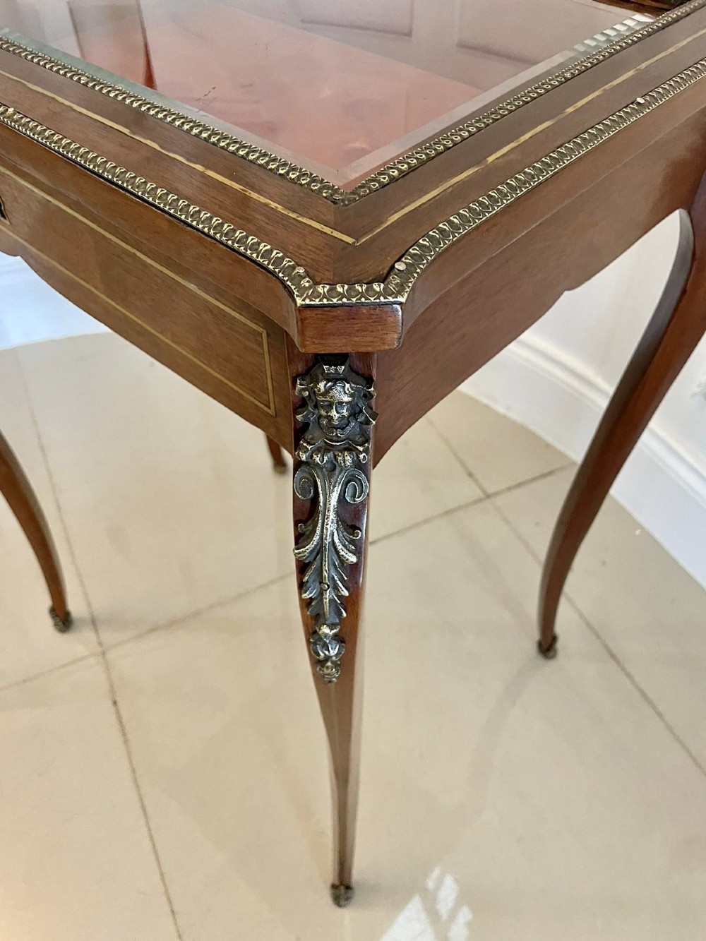 A 19th-century French mahogany bijouterie display table featuring a glazed top with brass inlay, a single front drawer, and slender cabriole legs with brass mounts. View VII
