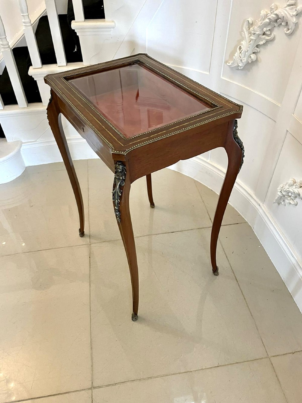 A 19th-century French mahogany bijouterie display table featuring a glazed top with brass inlay, a single front drawer, and slender cabriole legs with brass mounts. View IX