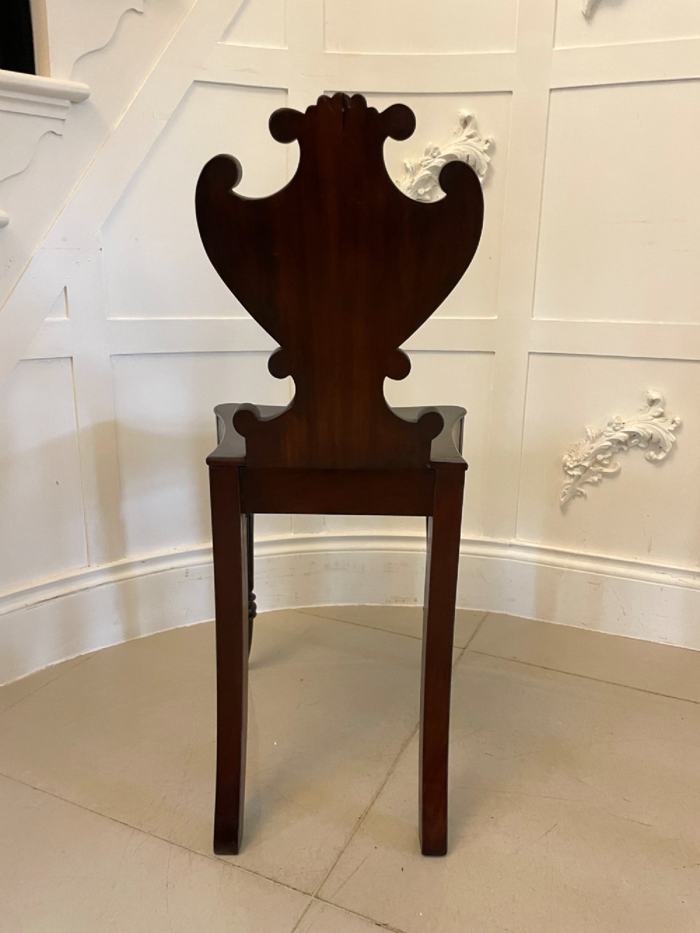 A pair of antique Regency dark mahogany hall chairs featuring scroll-carved cartouche backrests, solid timber seats, and reeded front legs. View III