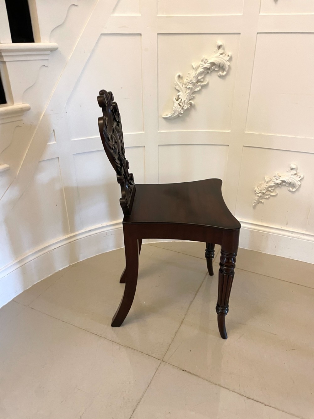 A pair of antique Regency dark mahogany hall chairs featuring scroll-carved cartouche backrests, solid timber seats, and reeded front legs. View IV