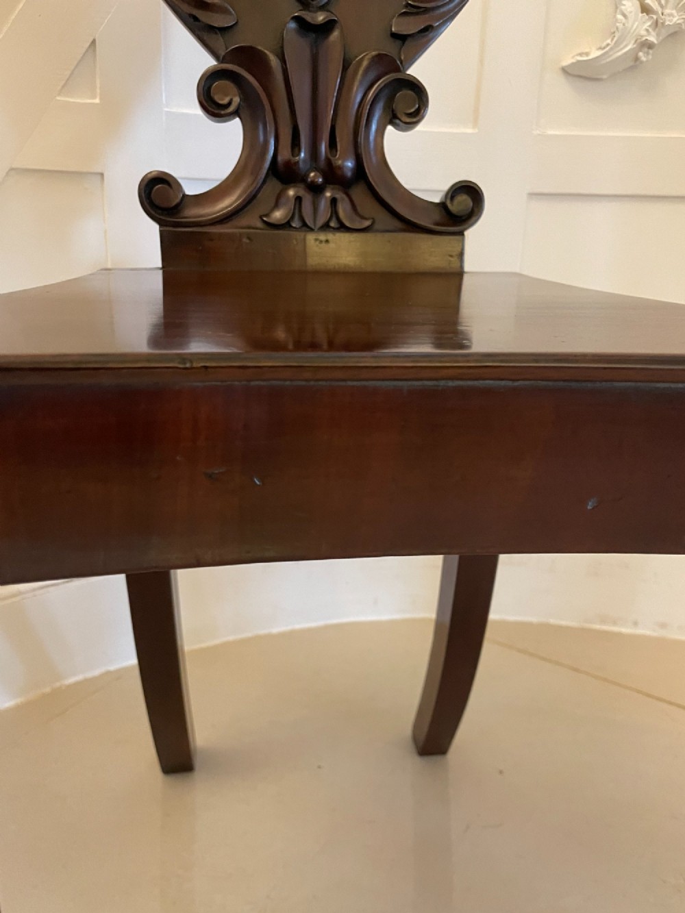 A pair of antique Regency dark mahogany hall chairs featuring scroll-carved cartouche backrests, solid timber seats, and reeded front legs. View V