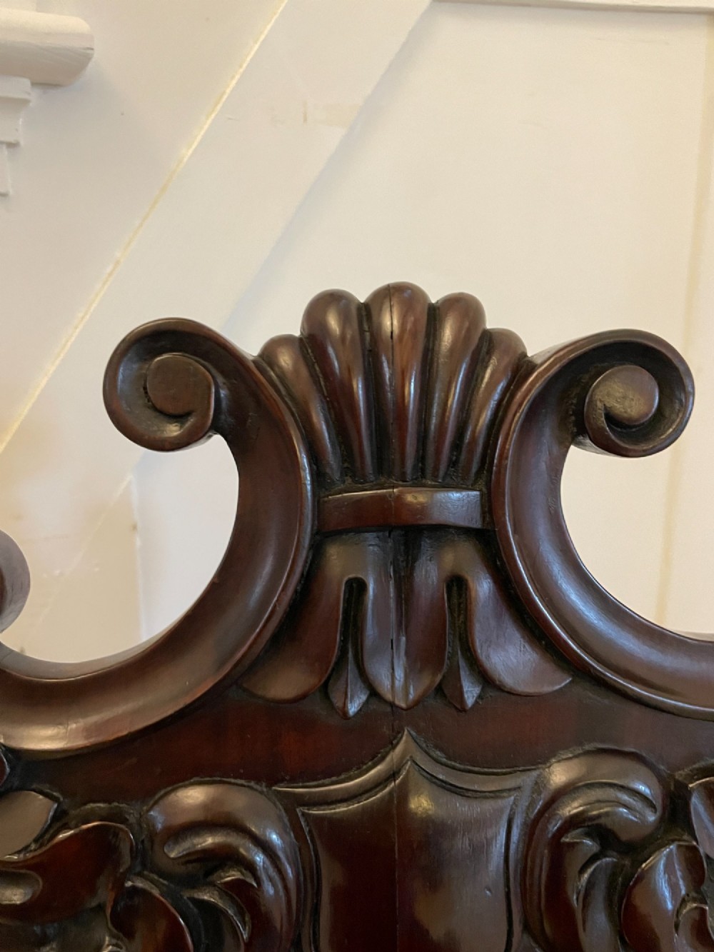 A pair of antique Regency dark mahogany hall chairs featuring scroll-carved cartouche backrests, solid timber seats, and reeded front legs. View X