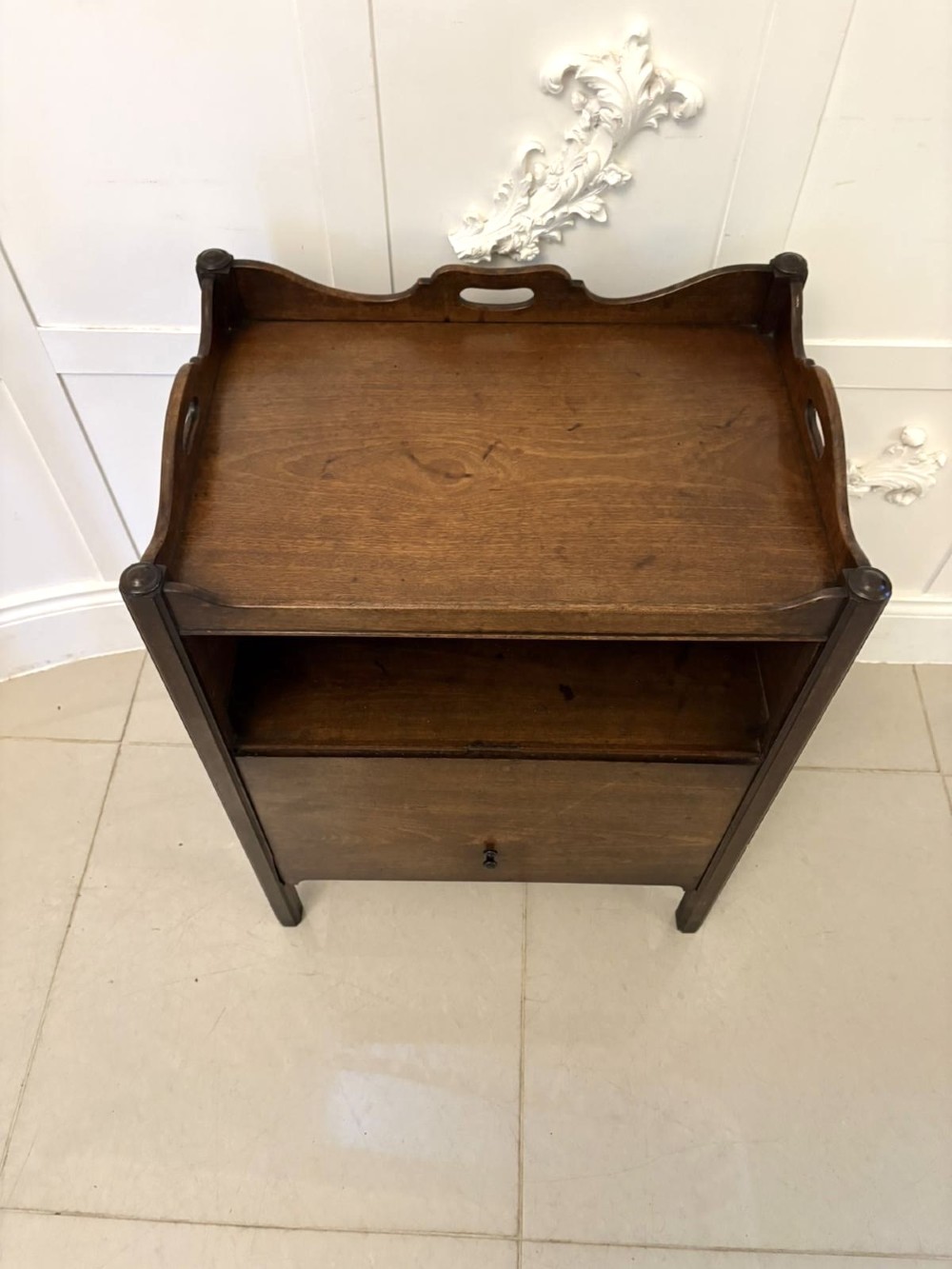 An 18th-century Georgian mahogany bedside cabinet featuring a gallery tray top with cut-out handles, a front cupboard door, and square legs. View V
