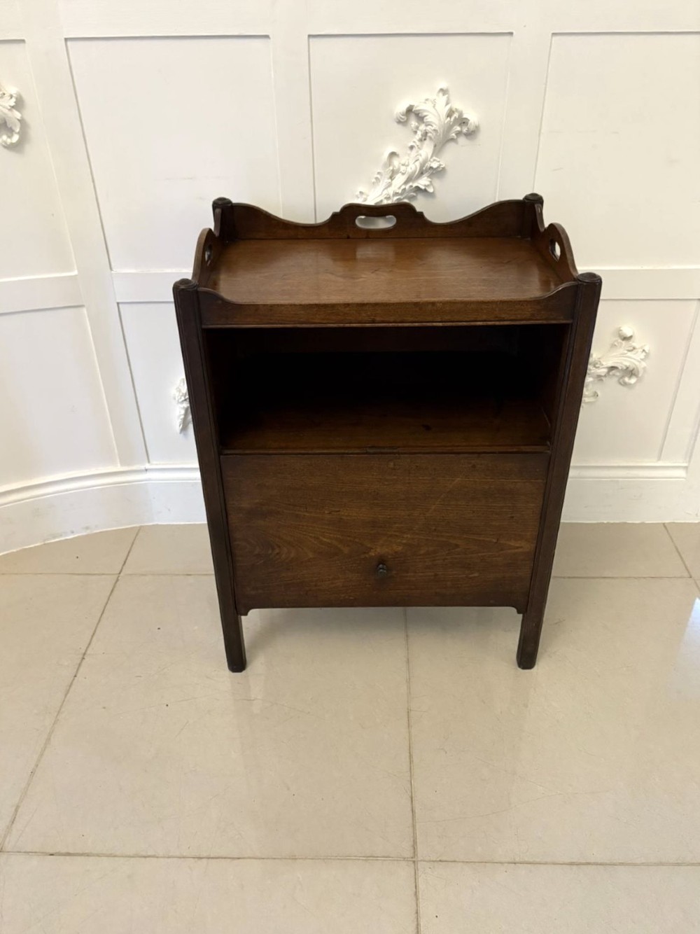 An 18th-century Georgian mahogany bedside cabinet featuring a gallery tray top with cut-out handles, a front cupboard door, and square legs. View VI