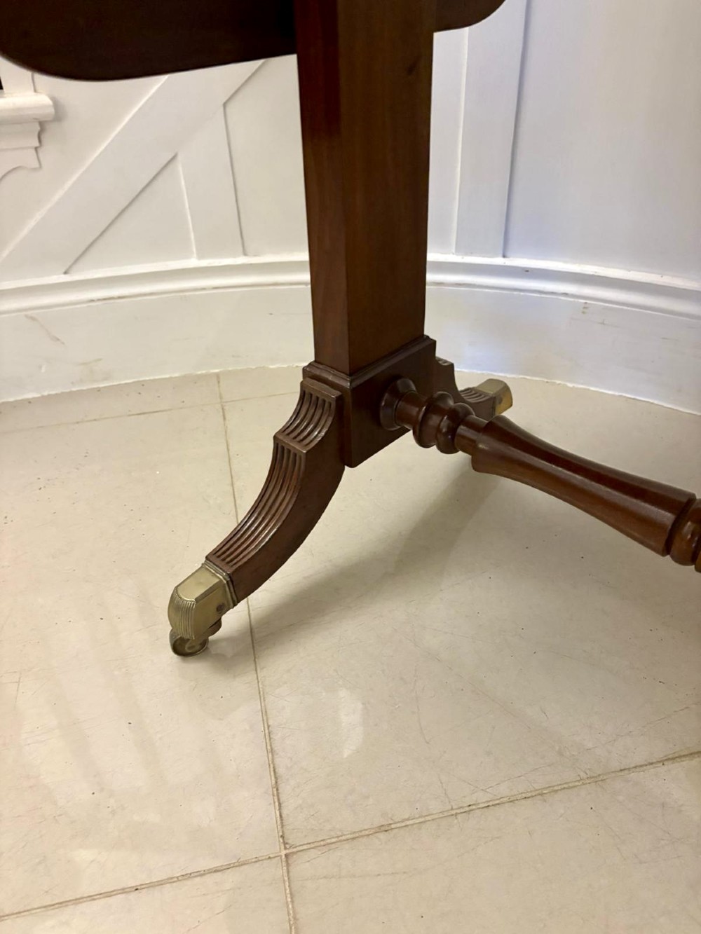 A Regency period mahogany sofa table featuring two drop-leaf sides, a single drawer with brass ring handles, reeded splayed legs, a turned stretcher bar, and brass castors. View IX