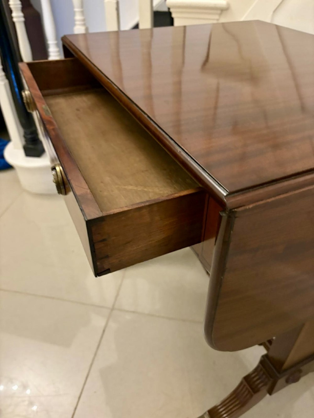 A Regency period mahogany sofa table featuring two drop-leaf sides, a single drawer with brass ring handles, reeded splayed legs, a turned stretcher bar, and brass castors. View XII