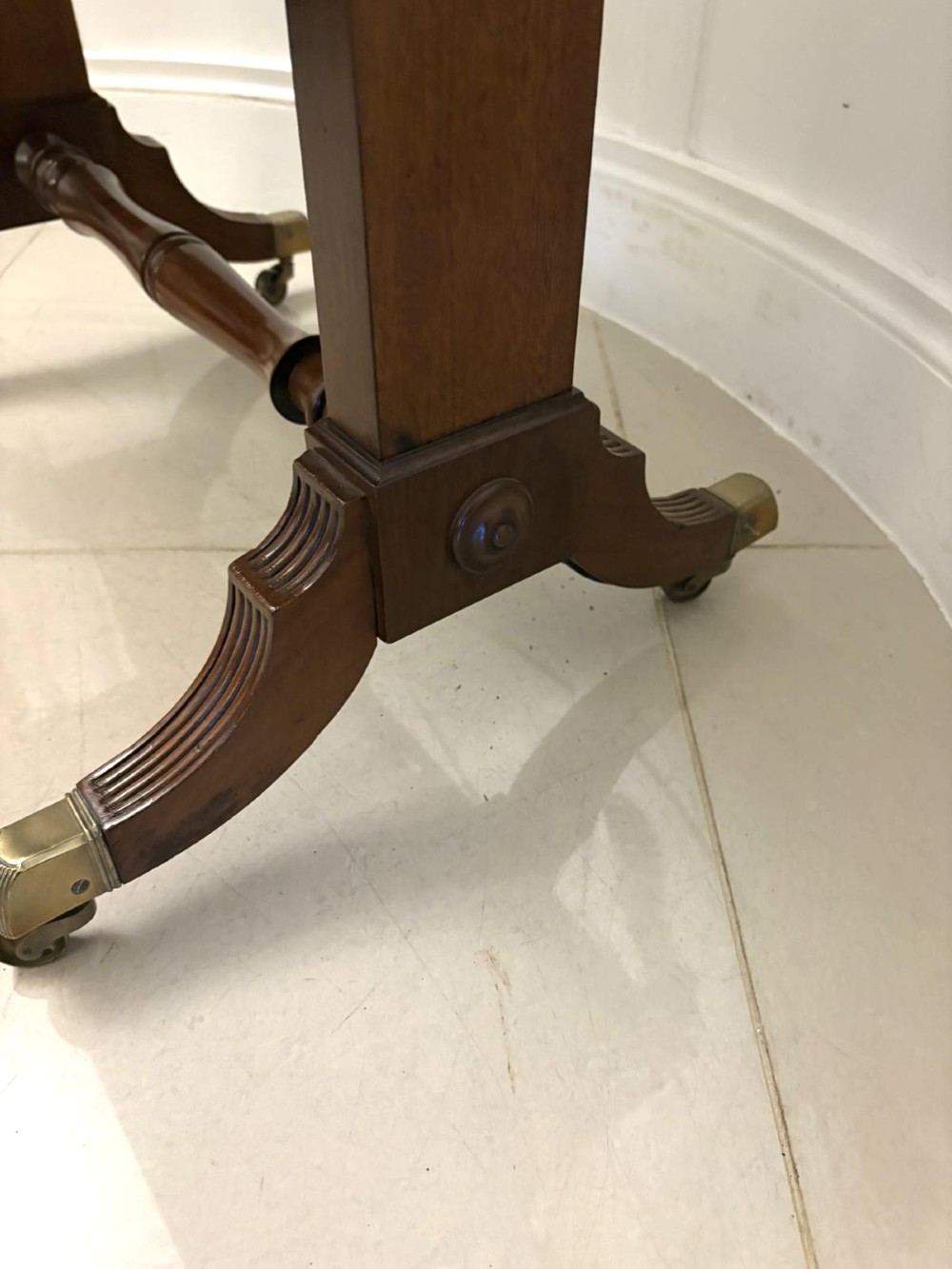 A Regency period mahogany sofa table featuring two drop-leaf sides, a single drawer with brass ring handles, reeded splayed legs, a turned stretcher bar, and brass castors. View XIII