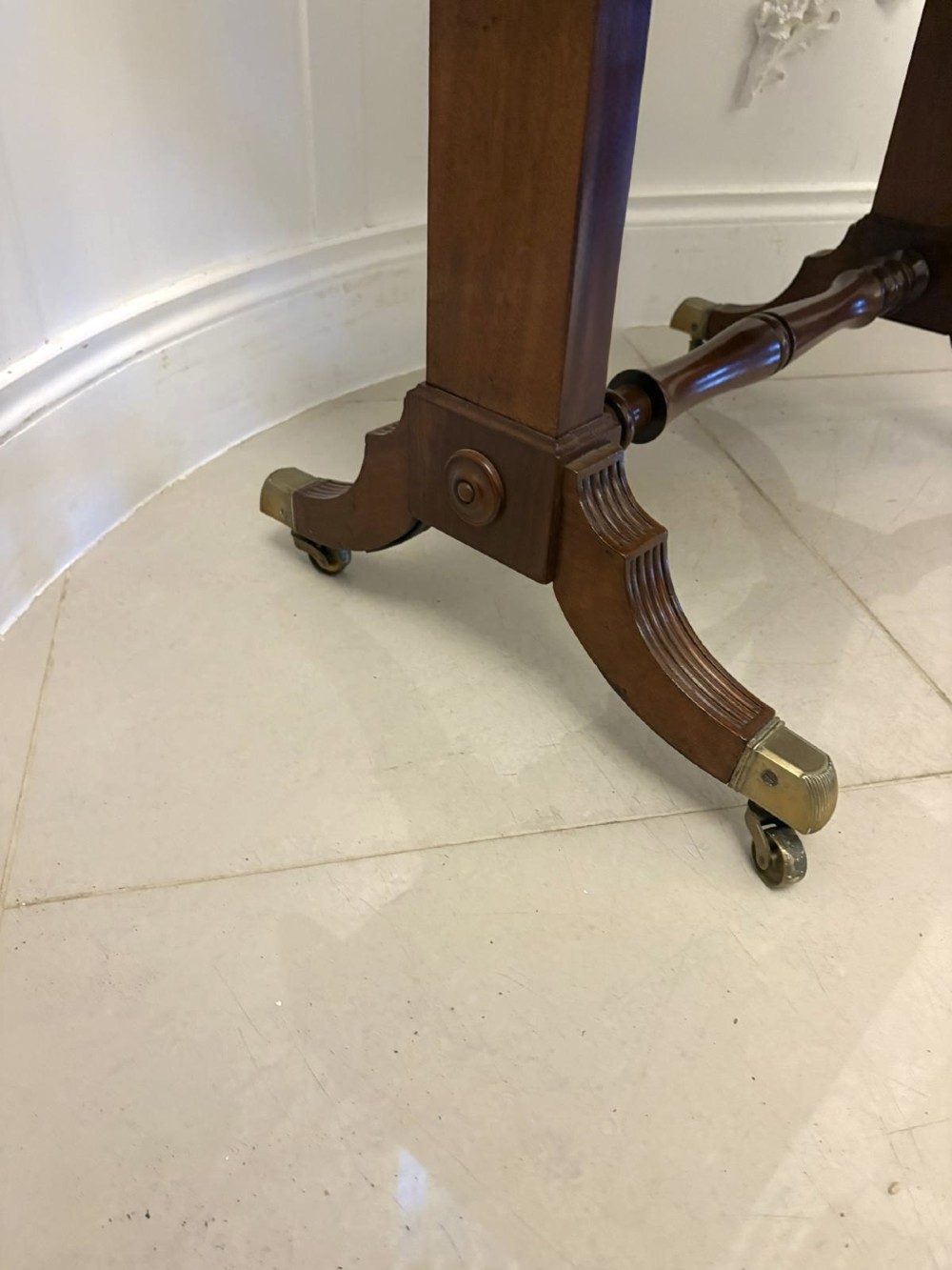 A Regency period mahogany sofa table featuring two drop-leaf sides, a single drawer with brass ring handles, reeded splayed legs, a turned stretcher bar, and brass castors. View XIV