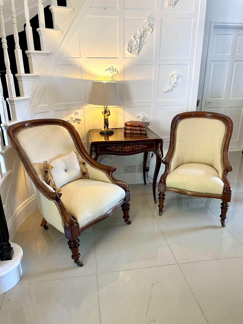 A pair of antique Victorian mahogany armchairs featuring carved show-frames, cream patterned upholstery, and turned front legs on castors. View V
