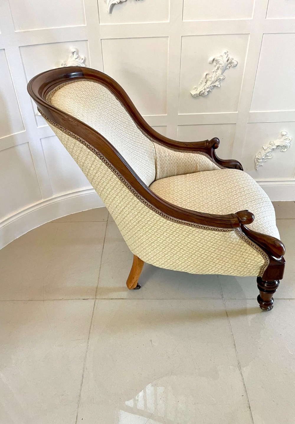 A pair of antique Victorian mahogany armchairs featuring carved show-frames, cream patterned upholstery, and turned front legs on castors. View VIII