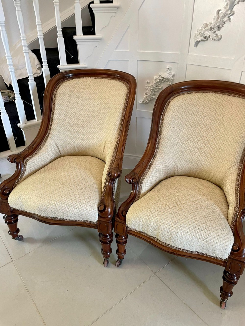 A pair of antique Victorian mahogany armchairs featuring carved show-frames, cream patterned upholstery, and turned front legs on castors. View XII
