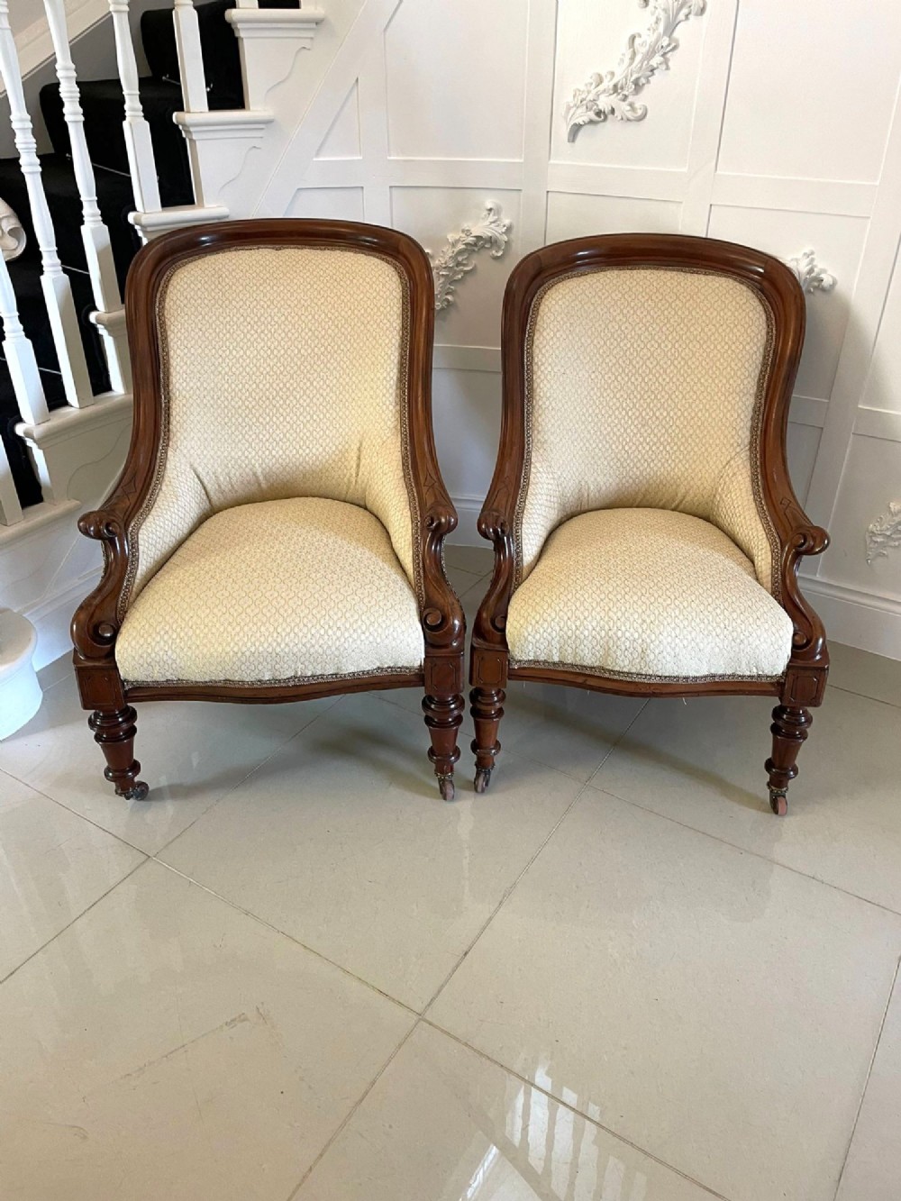 A pair of antique Victorian mahogany armchairs featuring carved show-frames, cream patterned upholstery, and turned front legs on castors. View XIII