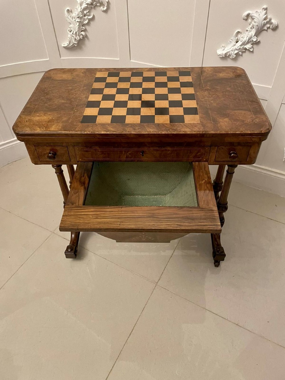 An antique Victorian burr walnut games table featuring an inlaid chessboard top, a frieze drawer, carved turned twin-column supports, and a pierced fretwork stretcher. View II